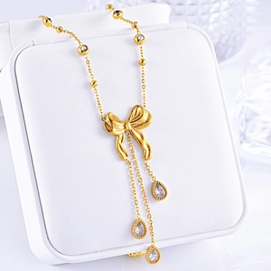 Detail of a gold necklace featuring a bow pendant and three white teardrop zircon tassels