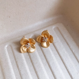 Macro detail of matte gold flower earrings with white zircon accents in French retro style