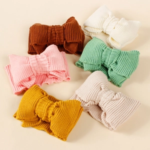 Flat lay of six colorful knitted baby headbands with large bows in a circular arrangement