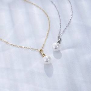 Detailed view of silver and gold pearl necklaces with zircon X-shape pendants on silk