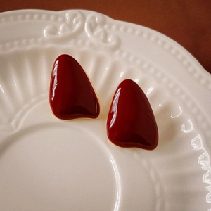Detail view of burgundy enamel teardrop earrings with gold edges on white ceramic tray