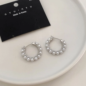 Detailed view of silver hoop earrings with white pearls on a white ceramic tray