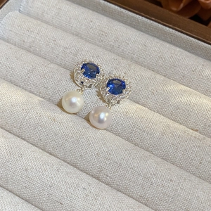 Dettaglio di orecchini con gemma blu, alone di diamanti e perle bianche pendenti