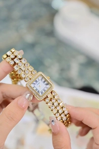 Close-up of golden rectangular watch with Roman numerals and gemstone bracelet strap