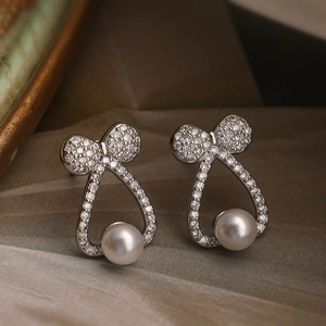 Orecchini a perno con fiocco in argento, zirconi e perle a goccia su sfondo vintage