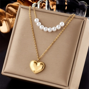 Double-layered gold necklace with heart pendant and pearls on a beige jewelry box