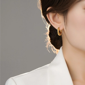 Close-up of minimalist gold hoop earring worn by model with metallic shine