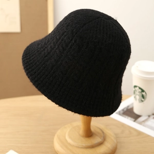 Black knit bucket hat with thick wool texture on a wooden head stand for winter