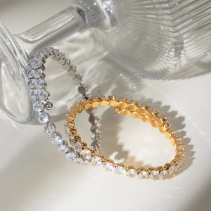 Detailed view of gold and silver zircon bracelets reflecting light near a glass