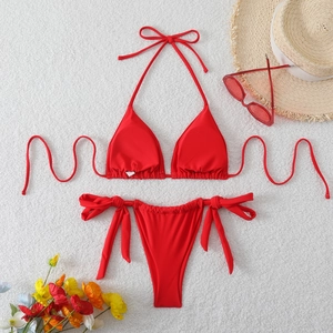 Dettaglio bikini rosso a triangolo con laccetti laterali su sfondo bianco testurizzato