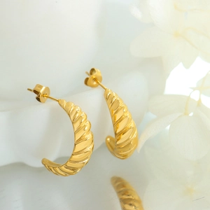 Goldene Creolen aus Titanstahl mit gedrehter Textur und Spiegelung bei weißen Blumen