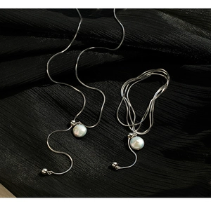 Macro detail of 925 silver snake chain with white pearl pendant on black textured fabric