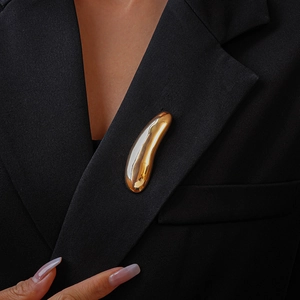Close-up of a polished golden liquid metal teardrop brooch on a black blazer lapel