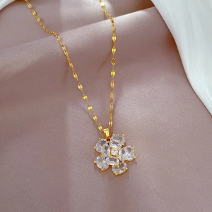 Macro shot of gold tone chain and flower pendant with clear zircon on pink satin background