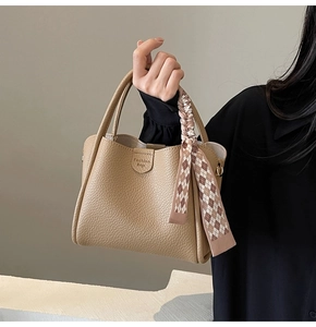 Detail of camel lychee grain leather bucket bag featuring a decorative silk scarf accessory