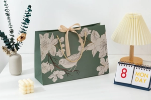 Green paper gift bag featuring elegant flower and bird patterns with beige ribbon bow