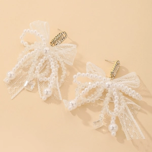 Détail des boucles d'oreilles nœud en dentelle avec perles et cristaux sur fond pêche