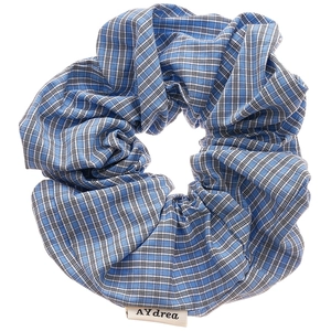 Blue and white checkered fabric scrunchie with brand logo tag on a clean white background