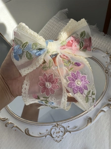 Close-up of a large lace bow hair clip with floral embroidery and mesh texture