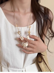 Detail of seashell and starfish pendant necklace worn by a model in a summer resort outfit