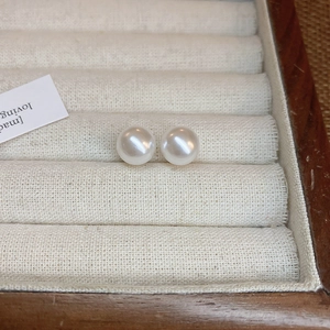 Elegant white pearl stud earrings on a white velvet display within a wooden frame box