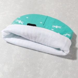 Detail of teal knit Christmas beanie featuring white patterns and soft folded cuff
