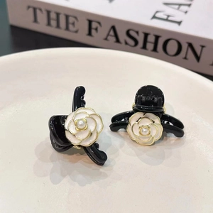 Close-up of mini camellia hair claw clips with gold trim and pearl centers on a plate