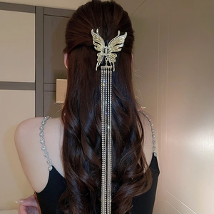 Détail d'une pince à cheveux papillon avec de longs glands et strass sur cheveux ondulés