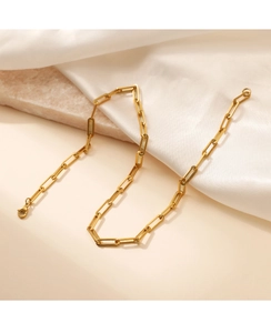 Detail of a golden paperclip chain necklace on silk and beige stone background