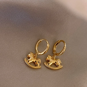 Detailed close-up of golden rocking horse earrings on elegant silk background