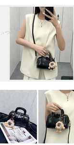 Detail of a black shiny Boston bag with gold hardware and a cute lion charm accessory