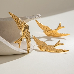 Vintage gold stainless steel swallow bird earrings set on a minimalist white stone surface