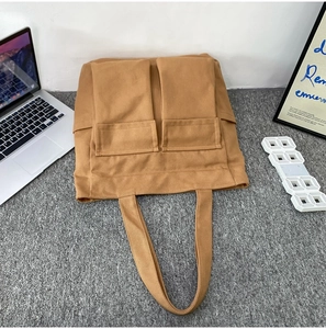 Close-up of tan canvas tote bag featuring dual front pockets and durable fabric texture