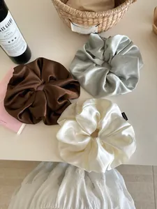 Close-up of three premium satin scrunchies in brown, silver-grey, and off-white colors