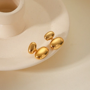 Dettaglio di orecchini a goccia ovali in oro lucido su un vassoio di ceramica beige