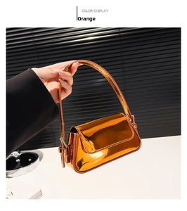 Detail of glossy orange patent leather baguette bag with adjustable strap and silver buckle