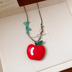 Détail du collier pendentif pomme rouge avec nœud à carreaux verts sur tissu doux