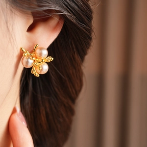 Close-up of elegant pearl flower earrings with gold leaf accents on model's ear