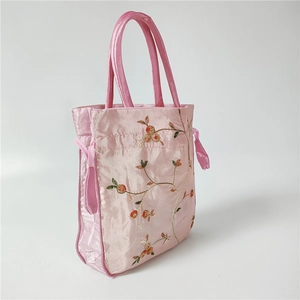 Close-up of floral embroidery on pink satin handbag with silk drawstring closure