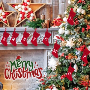 Red knitted Christmas stocking with white letter and pet paw print hanging on a fireplace
