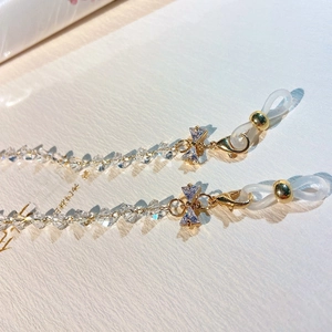 Detail of transparent crystal chain with golden bow accent and zircon stones for eyewear