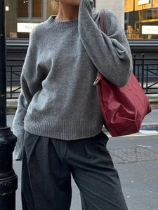 Street style view of grey round neck long sleeve knit sweater paired with a handbag
