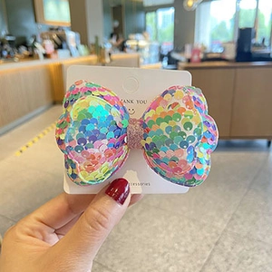 Detailed view of handmade rainbow sequin bow hair clip with sparkling texture on card