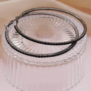 Detailed view of oversized black crystal hoop earrings on a decorative glass stand