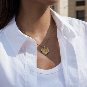 Detail of a gold heart pendant with red gem and white crystals on a woman neck