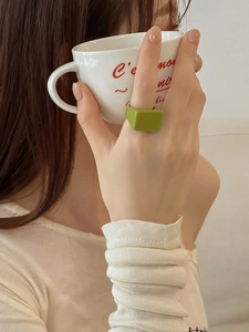 Détail d'une bague carrée en résine verte portée par un mannequin tenant une tasse de café