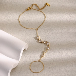 Chaîne de main élégante plaquée or 18K avec zircons gouttes sur fond texturé beige