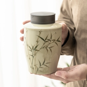 Ceramic tea canister with bamboo pattern and alloy lid held by hands in natural light