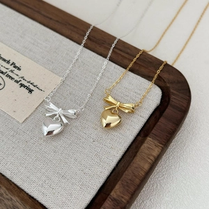 Close-up of gold and silver bow heart necklaces on a rustic wooden jewelry tray