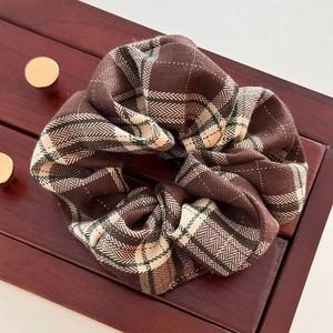 Detail view of a vintage dark brown plaid scrunchie on a dark wood storage surface